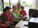 During the Cascadia Rising earthquake exercise in the Pacific Northwest, Island County Amateur Radio Club members John Acton, K7ACT (seated, in yellow vest), types a Red Cross emergency message via a 2 meter packet link, while Bill Frederick, KF7BMK (standing, with handheld), monitors a VHF simplex voice net at a field triage and treatment facility on Whidbey Island. Red Cross volunteers Kendra O'Bryan (left) and Patty Cheek (right) help coordinate the message traffic flow. [Vince Bond, K7NA, photo]